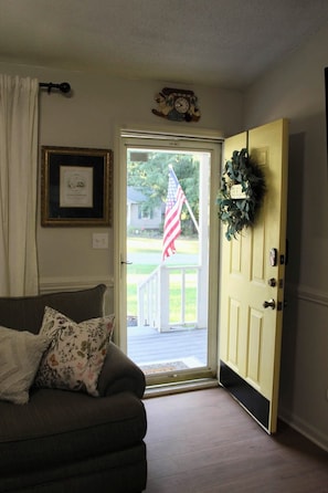 Een woonkamer met een bank, een deur versierd met een krans, een Amerikaanse vlag en een ingelijst certificaat aan de muur.