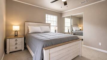 A bedroom with a bed, nightstand, lamp, ceiling fan, and a large mirror.