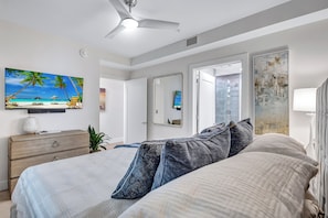 A bedroom with a bed, a dresser, a ceiling fan, a painting of a beach, a mirror, and a window. - Luxury Bayfront Designer Retreat • Paddleboard • Stunning Sarasota Sunsets (Sarasota)