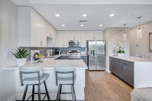 A modern kitchen with white cabinetry, stainless steel appliances, a central island with bar stools, and pendant lighting. - Luxury Bayfront Designer Retreat • Paddleboard • Stunning Sarasota Sunsets (Sarasota)
