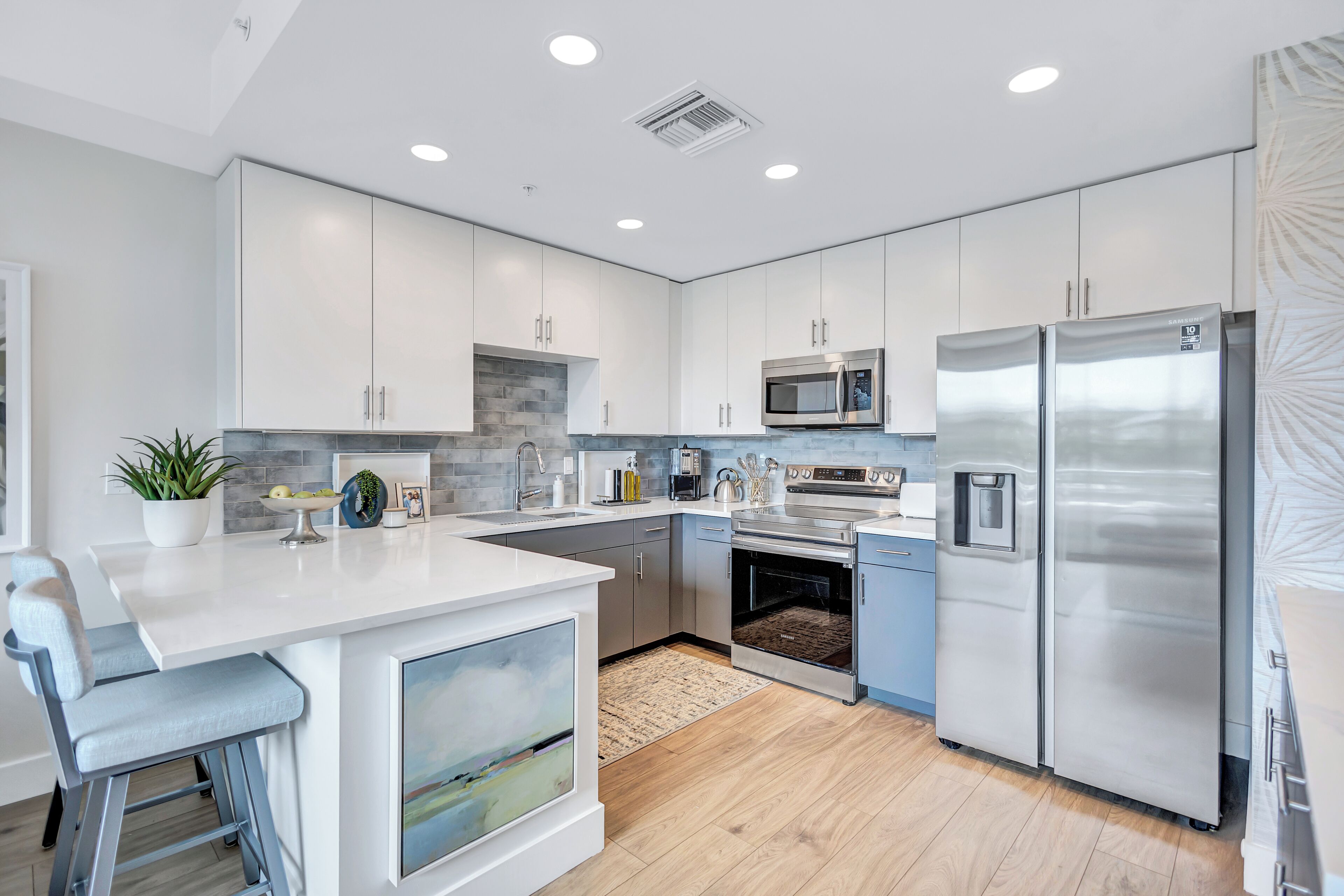 A modern kitchen with white cabinetry, stainless steel appliances, and a bar area with stools.