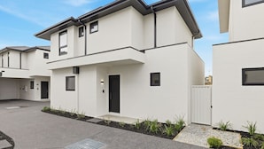 A modern two-story residential building with a flat roof, a front door, and a small window on the second floor. - Domi Rentals - The Cheltenham Southland House (Cheltenham)