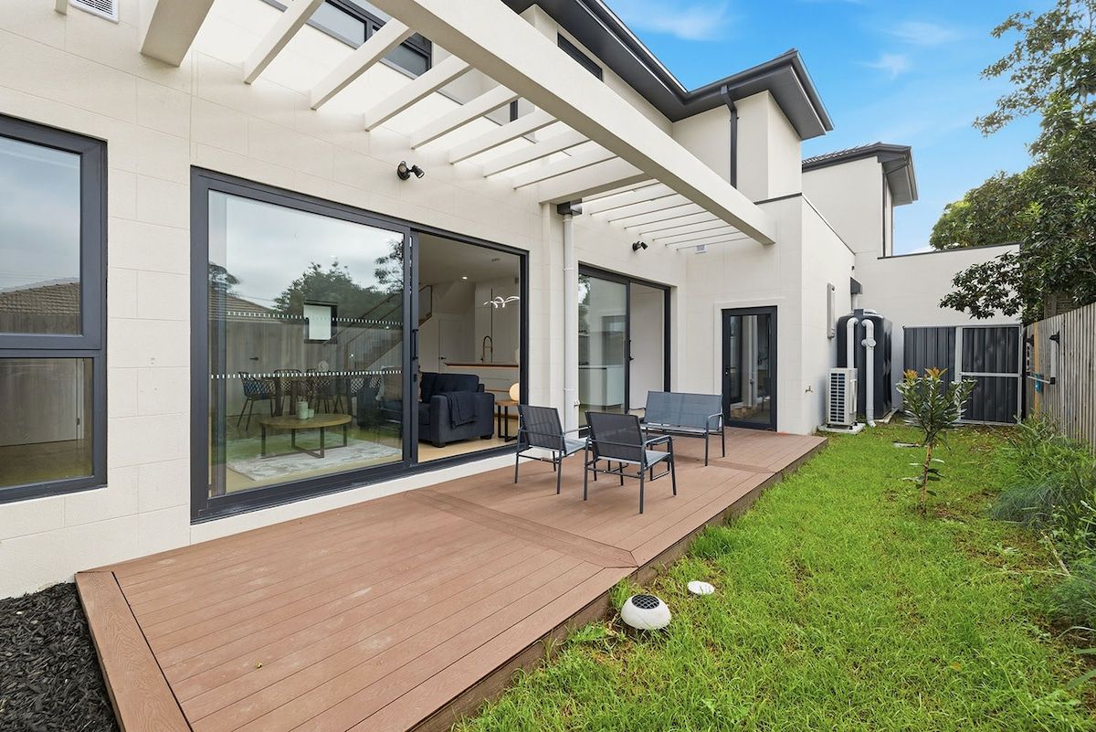 Een modern huis met een terras, buitenmeubels en een overdekt gedeelte.