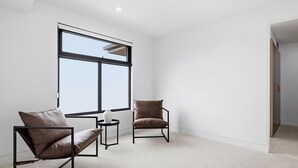 A modern room with a large window, two leather chairs, a small round table, and a white vase. - Domi Rentals - The Cheltenham Southland House (Cheltenham)