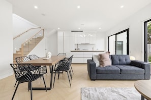 A modern interior with a dining area, sofa, and staircase. - Domi Rentals - The Cheltenham Southland House (Cheltenham)
