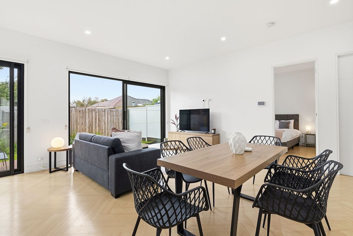 A modern living space with a dining area, sofa, TV, and a bedroom.