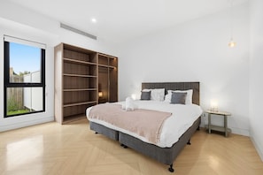 A bedroom with a large bed, a wardrobe, a bedside table, and a window. - Domi Rentals - The Cheltenham Southland House (Cheltenham)