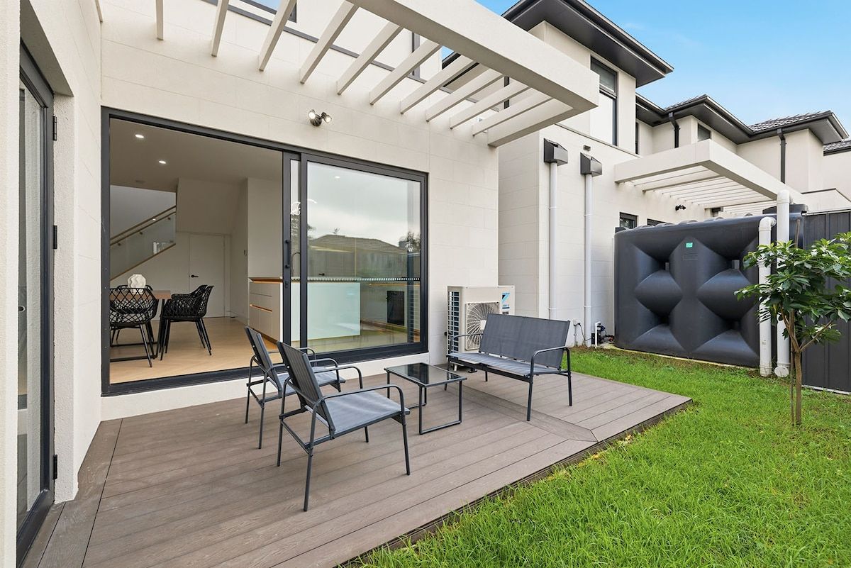 A modern patio with outdoor furniture, a glass door entrance, and a covered area with a cushioned seating arrangement.