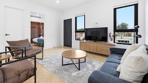 Un salon moderne avec un canapé, une table basse, un téléviseur et une vue sur l’extérieur.