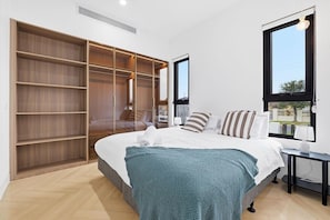A bedroom with a large bed, a wardrobe, and a window. - Domi Rentals - The Cheltenham Southland House (Cheltenham)