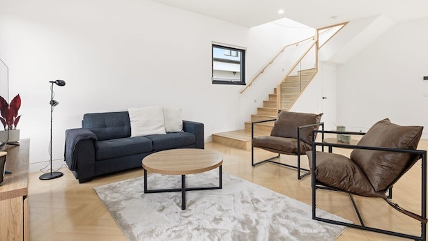 Un salon moderne avec un canapé, une table basse et des fauteuils, un escalier et une grande fenêtre.