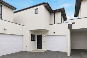 A modern two-story building with a flat roof, white exterior walls, and a central entrance with a black door. - Domi Rentals - The Cheltenham Southland House (Cheltenham)