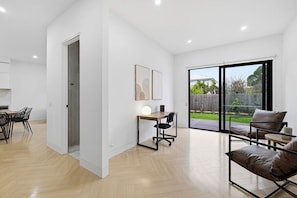 A spacious living area with a dining set, a work desk, and a comfortable seating area. - Domi Rentals - The Cheltenham Southland House (Cheltenham)