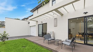 Ein modernes Haus mit überdachter Terrasse, Garage und Essbereich mit Gartenmöbeln.