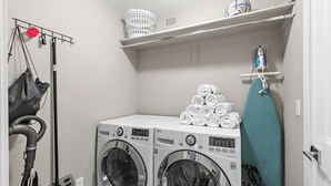 A laundry area with two front-loading washing machines, a drying rack, and a hanging rack with a red item. - Desert Rendezvous at Estancia Resort (Saint George)