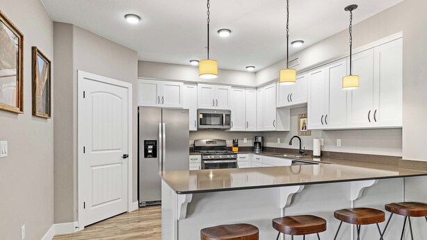 A modern kitchen with white cabinets, stainless steel appliances, a large island with stools, and pendant lighting. - Desert Rendezvous at Estancia Resort (Saint George)