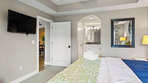 A bedroom with a bed, a TV, a mirror, and a door leading to a bathroom. - Desert Rendezvous at Estancia Resort (Saint George)