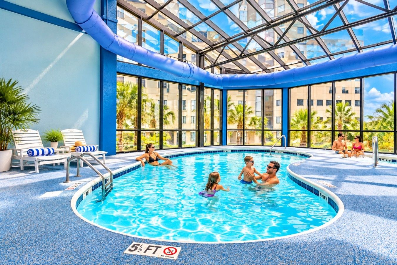 En inomhuspool med ett glastak, solstolar och en skylt som förbjuder dykning.