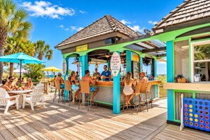 A tropical bar with a wooden deck, outdoor seating, and a sign advertising tropical drinks. - Beach Cove Resort - Direct Oceanfront Balcony with Pools (North Myrtle Beach)