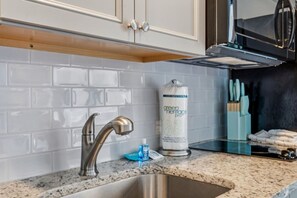 Cozinha com pia de aço inoxidável, painel de azulejos brancos e um rolo de papel toalha verde.