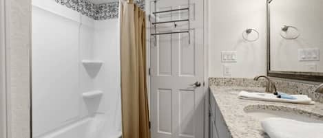 A bathroom with a bathtub, a shower curtain, a towel rack, a sink with a mirror, and a towel.