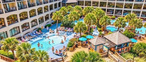 A hotel with a large outdoor pool surrounded by palm trees and lounge chairs.