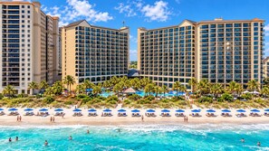 Ein Strandhotel mit mehreren Hochhäusern, einem Poolbereich und einem Strand mit Liegestühlen.