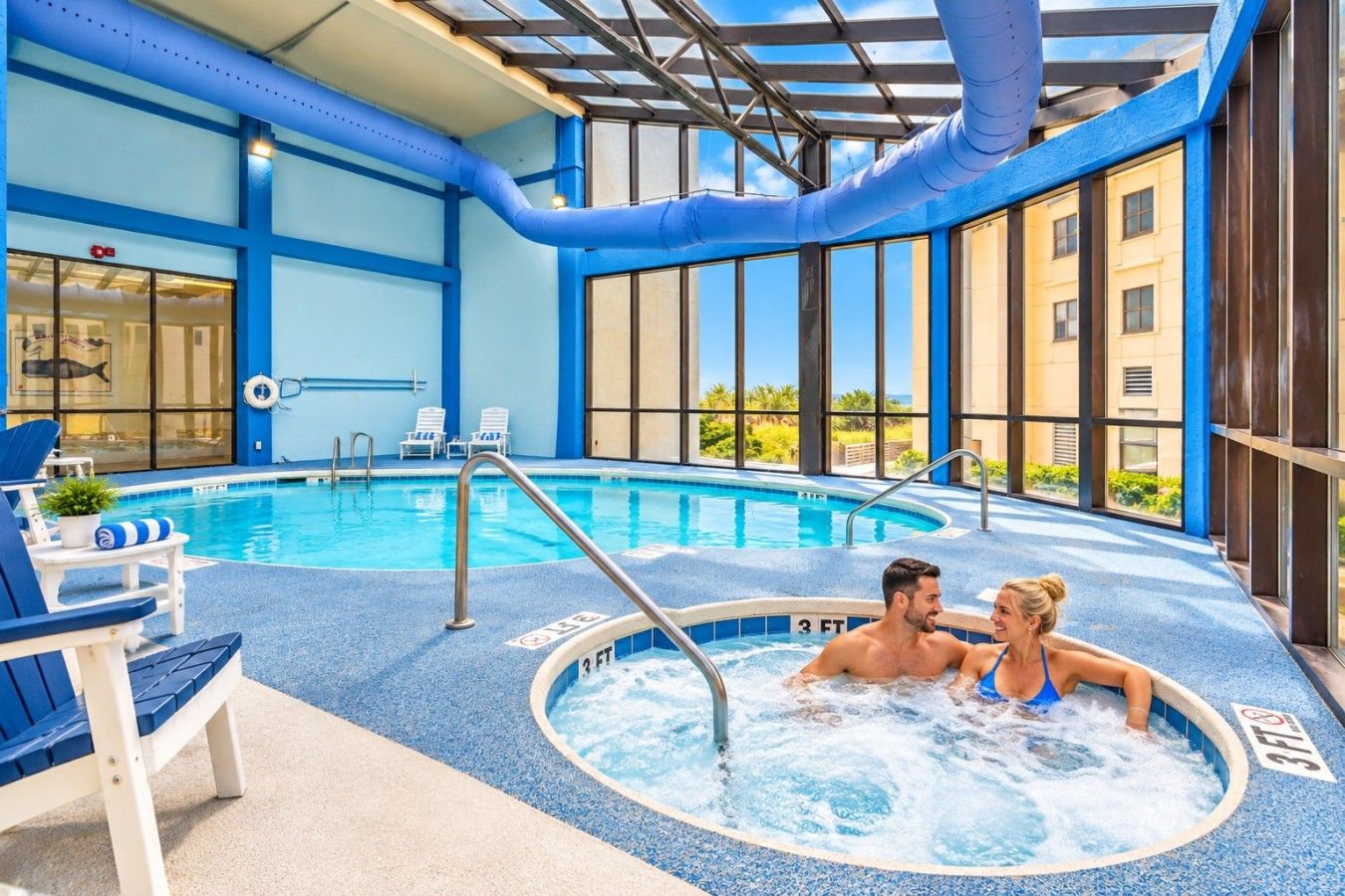 Piscina interna com hidromassagem, espreguiçadeiras e vista para o exterior.