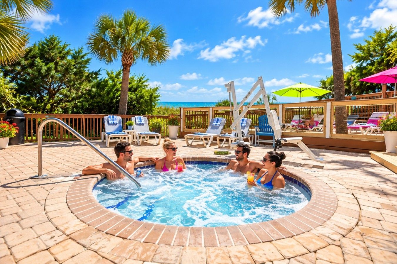 A hot tub surrounded by lounge chairs and umbrellas, with a poolside setting and palm trees.