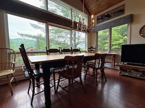 A dining area with a large wooden table and chairs, a chandelier, and a television on a stand. - W38: Spacious 5BR Slope-View Retreat | Ping Pong, Fireplace & Bretton Woods Adventure (Bretton Woods)
