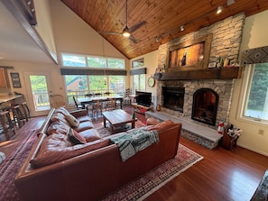 A spacious living room with a stone fireplace, leather sofas, a dining area, and large windows. - W38: Spacious 5BR Slope-View Retreat | Ping Pong, Fireplace & Bretton Woods Adventure (Bretton Woods)