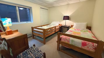 A room with two wooden beds, a desk with a lamp, a chair, and a window with blinds.