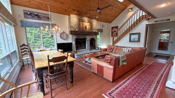 A spacious living area with a fireplace, wooden flooring, a dining table with chairs, a sofa, and a staircase.