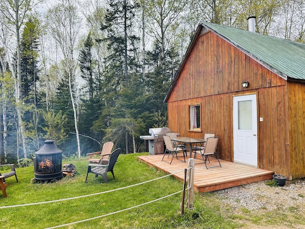 A wooden cabin with a deck, a grill, and a fire pit.