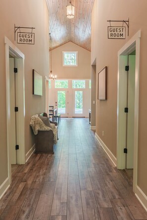 A hallway with wooden flooring, a couch, and two signs indicating guest rooms. - Scout's Retreat (Green Township)