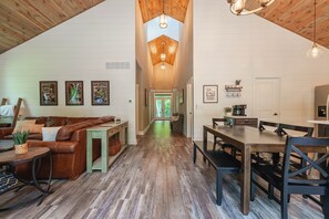 A spacious loft with a high ceiling, a dining area, a living room with a sofa and coffee table, and a kitchen area. - Scout's Retreat (Green Township)