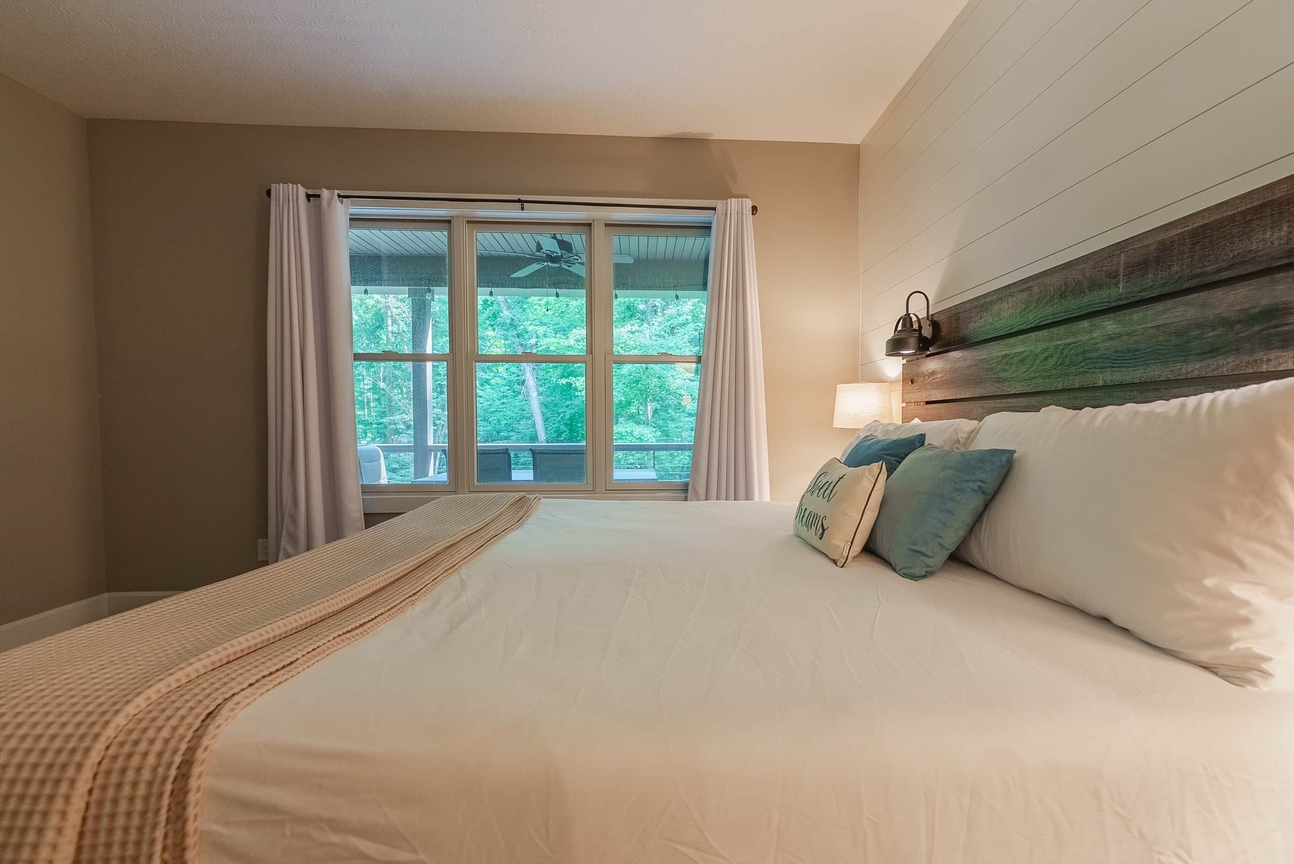 Una camera da letto con un letto grande, una finestra con tende, un ventilatore a soffitto e una testiera in legno.