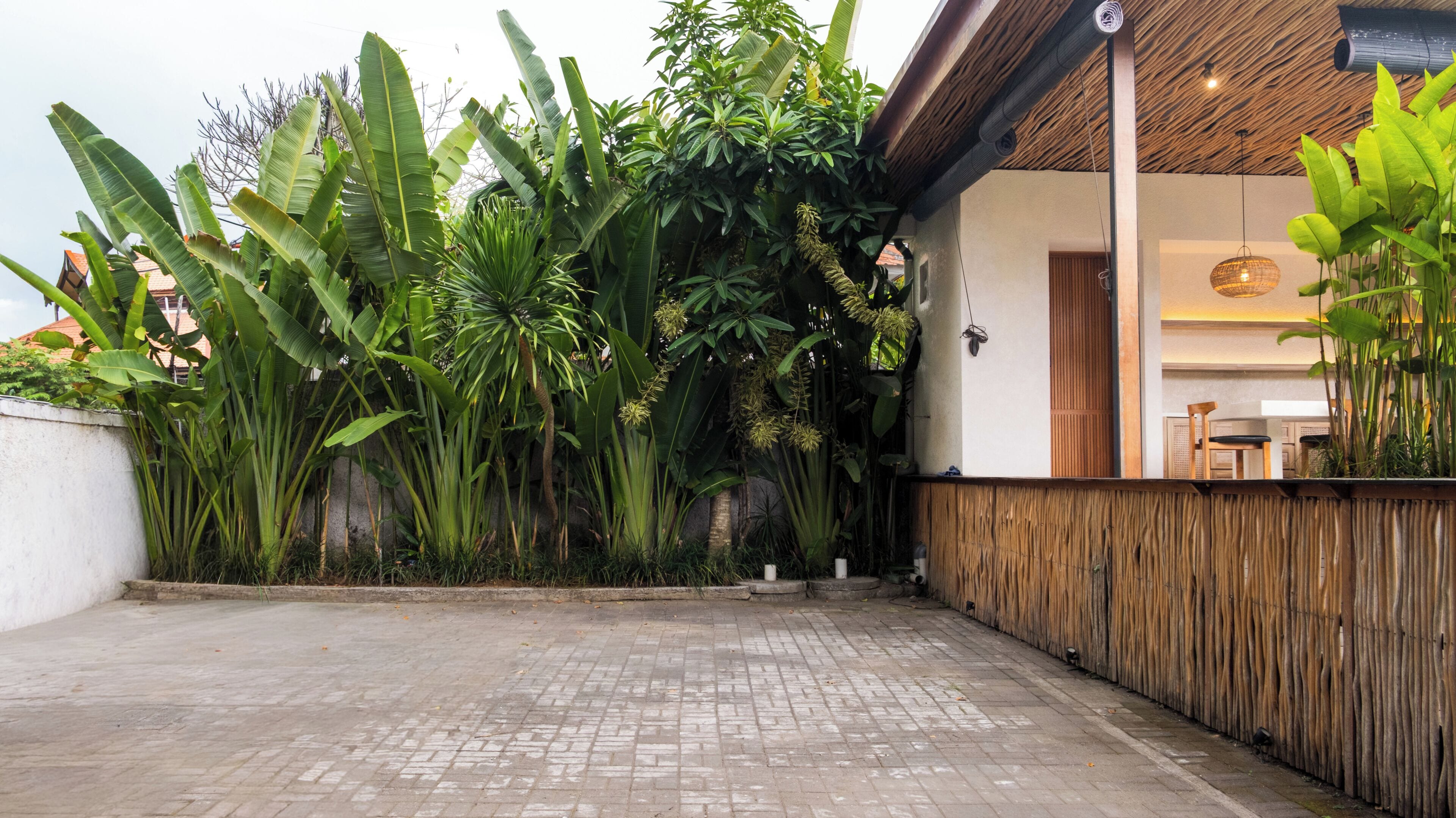 Un patio con piso de ladrillo, cerca de bambú y exuberante vegetación tropical.