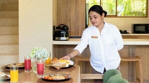 A person serving breakfast on a wooden table with various dishes, including toast, eggs, and a croissant. - Lexington Palace Villa (Bali)