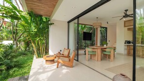 Een modern interieur met een glazen deur naar een eetgedeelte, omgeven door weelderige begroeiing.