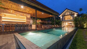Ein Poolbereich mit Bar, Liegestühlen und einem modernen Haus mit großen Fenstern.
