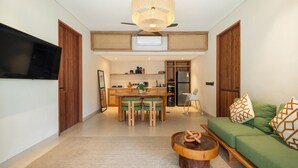 Ein modernes Wohnzimmer mit Essbereich, einer Küche im Hintergrund und einem grünen Sofa mit gemusterten Kissen.