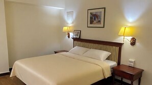 Camera d'hotel con un letto, abat-jour, comodino, un quadro incorniciato al muro e pavimento in legno.