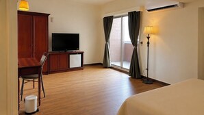 Una camera d'albergo con un letto, una televisione, una scrivania con una sedia, una lampada e una finestra con tende.