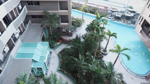 Un edificio a più piani con una piscina circondata da palme e una formazione rocciosa.