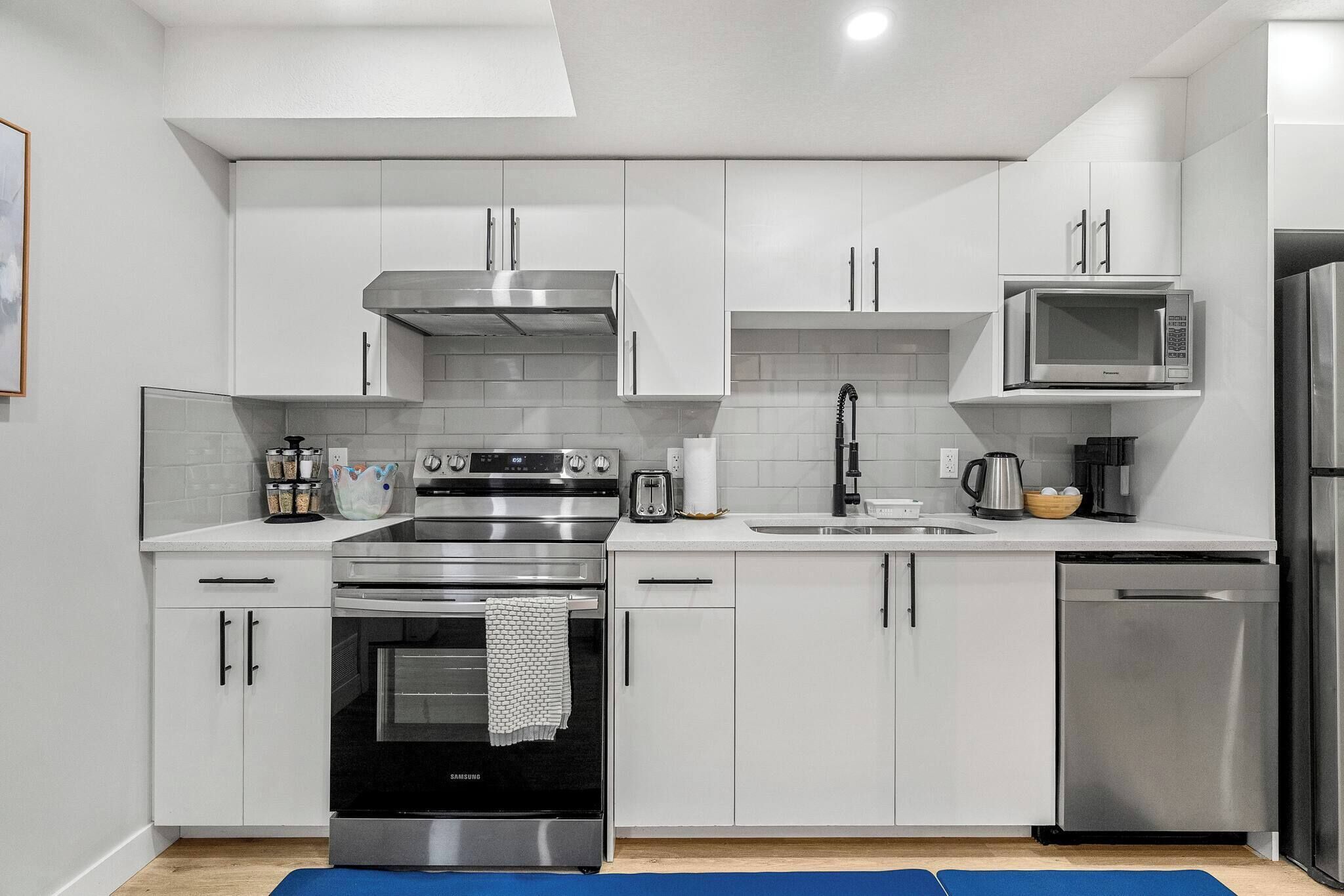 A modern kitchen with stainless steel appliances, white cabinetry, and a blue rug on the floor.