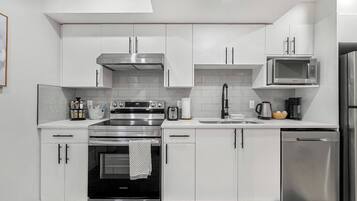 A modern kitchen with stainless steel appliances, white cabinetry, and a blue rug on the floor.