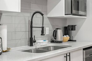 Una cocina con un grifo moderno, un lavamanos de acero inoxidable y una tetera sobre la encimera.