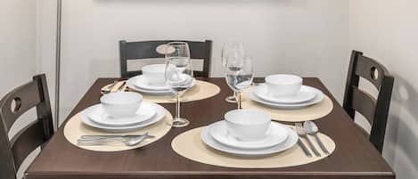 A dining table set with white plates, bowls, and cutlery, accompanied by two wine glasses.