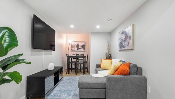 A modern living room with a grey sofa, a flat-screen TV, a dining table with chairs, and a blue patterned rug. - Latobir Modern,stylish 2BR Suite Private Entrance (Calgary)